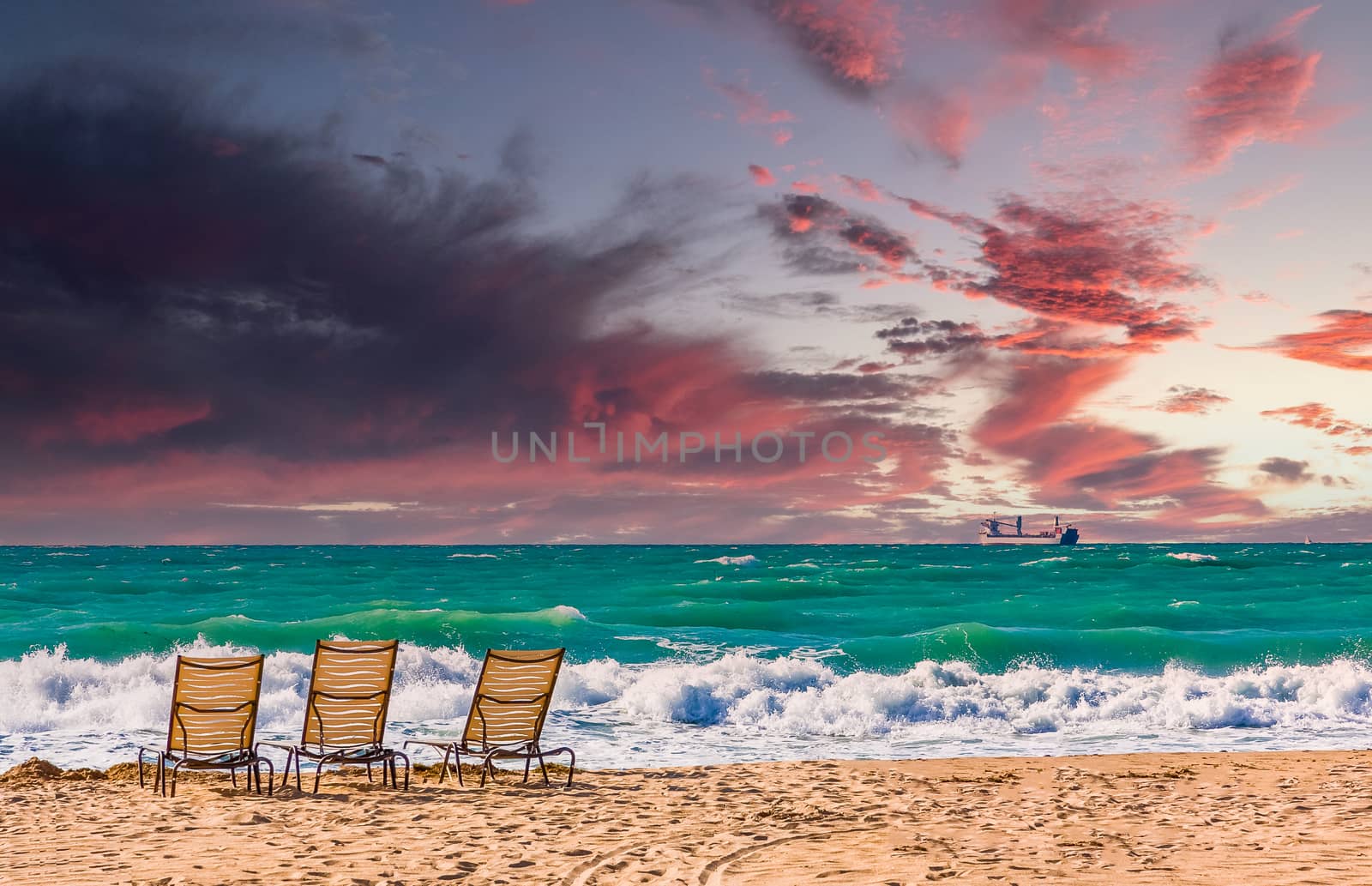 Chaise Lounges on an empty beach under cloudy skies with a freighter out to see