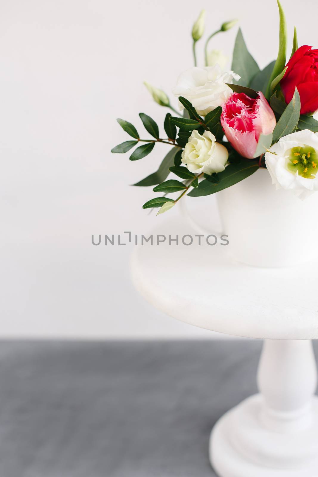 Spring bouquet in white vase on wooden white stand. Roses, tulips and lisianthus