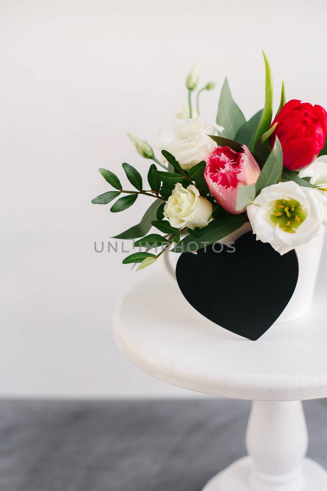 Black board heart copyspace. Spring bouquet in white vase on wooden white stand. Roses, tulips and lisianthus. by Denys_N