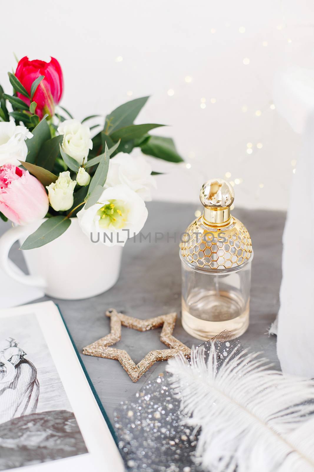 Bottle of perfume. Spring bouquet on gray concrete table. Roses, tulips and lisianthus. White feather