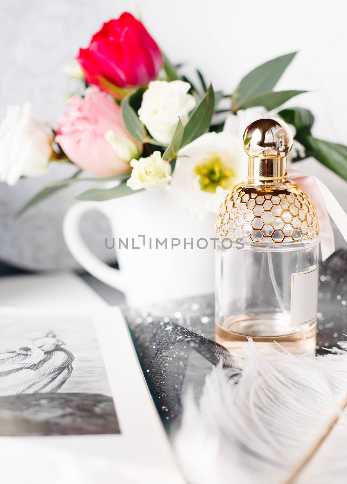Bottle of perfume. Spring bouquet on gray concrete table. Roses, tulips and lisianthus. White feather