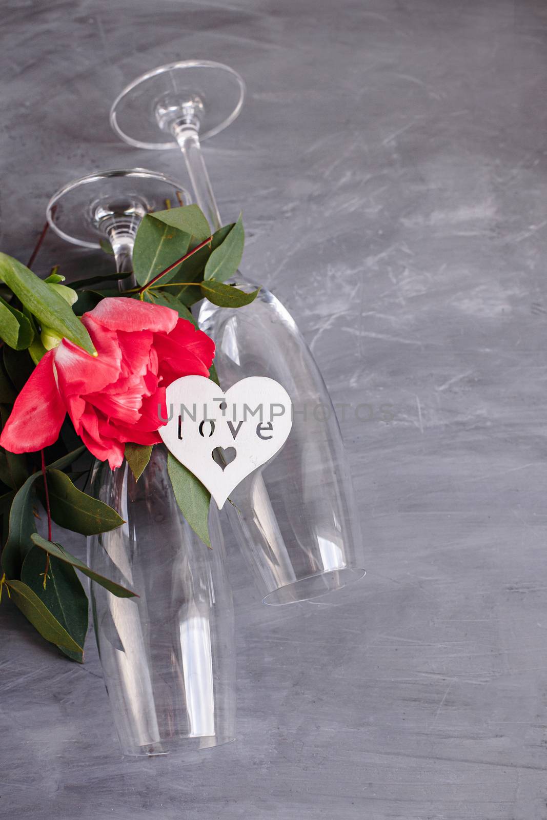 Composition with glass for champagne. Flowers and hearts on grey concrete background