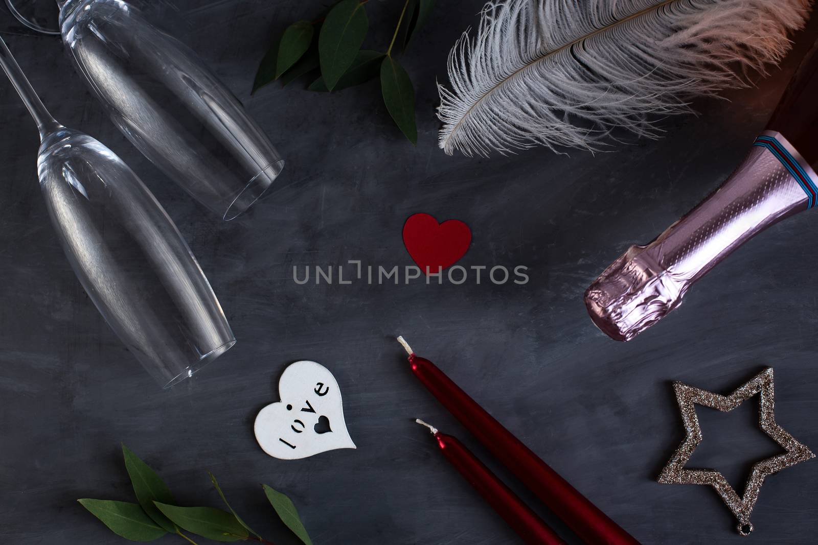 Flat lay composition with bottle of champagne, candles, feather and hearts for celebration on grey concrete background. Glass for champagne