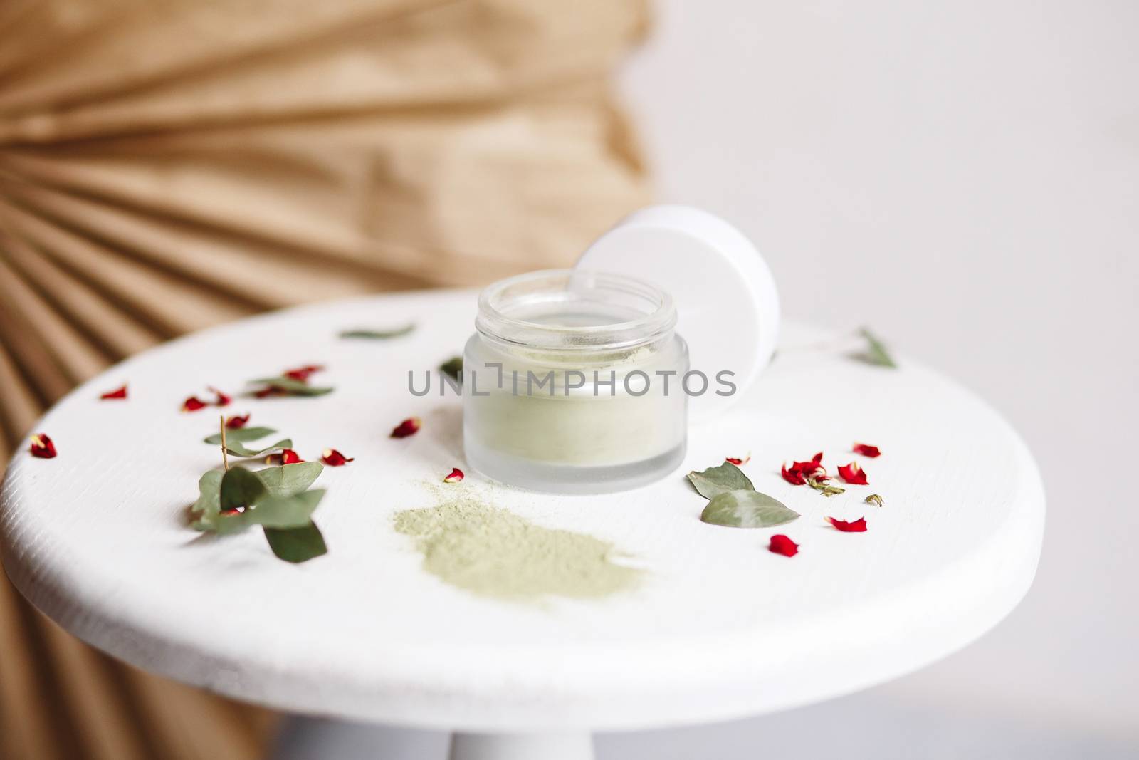 Powder cosmetic mask. Glass jar with matcha on a white background with dry petals