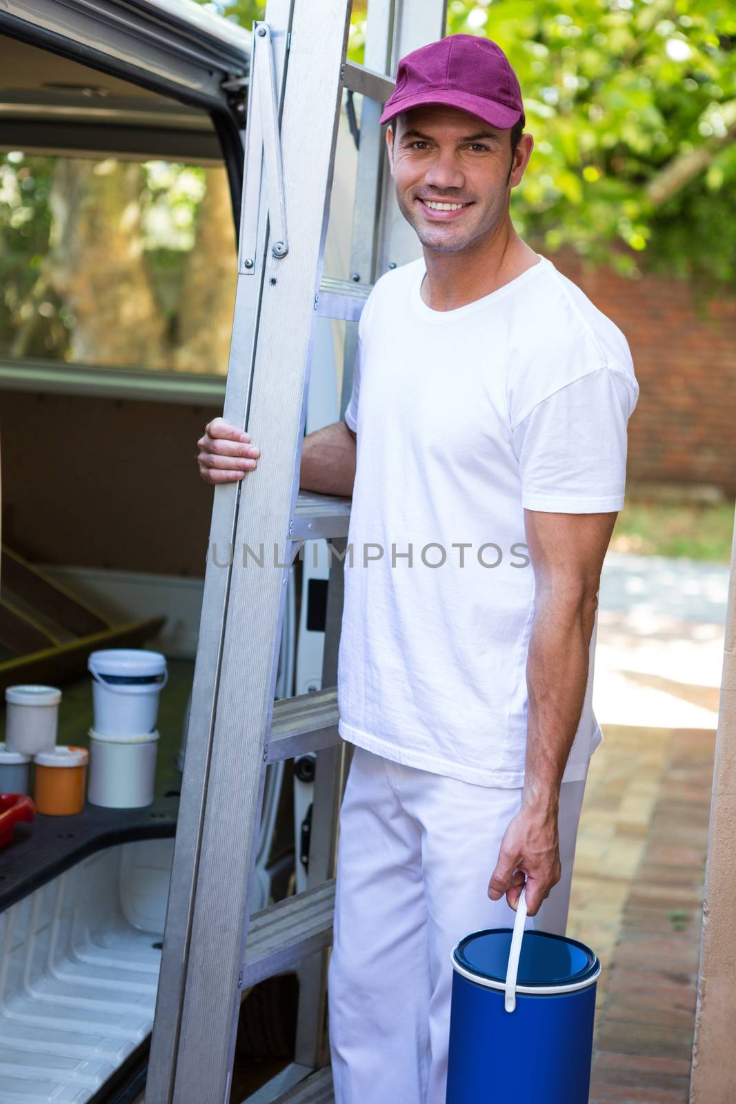Portrait of painter holding stepladder and bucket standing near his van