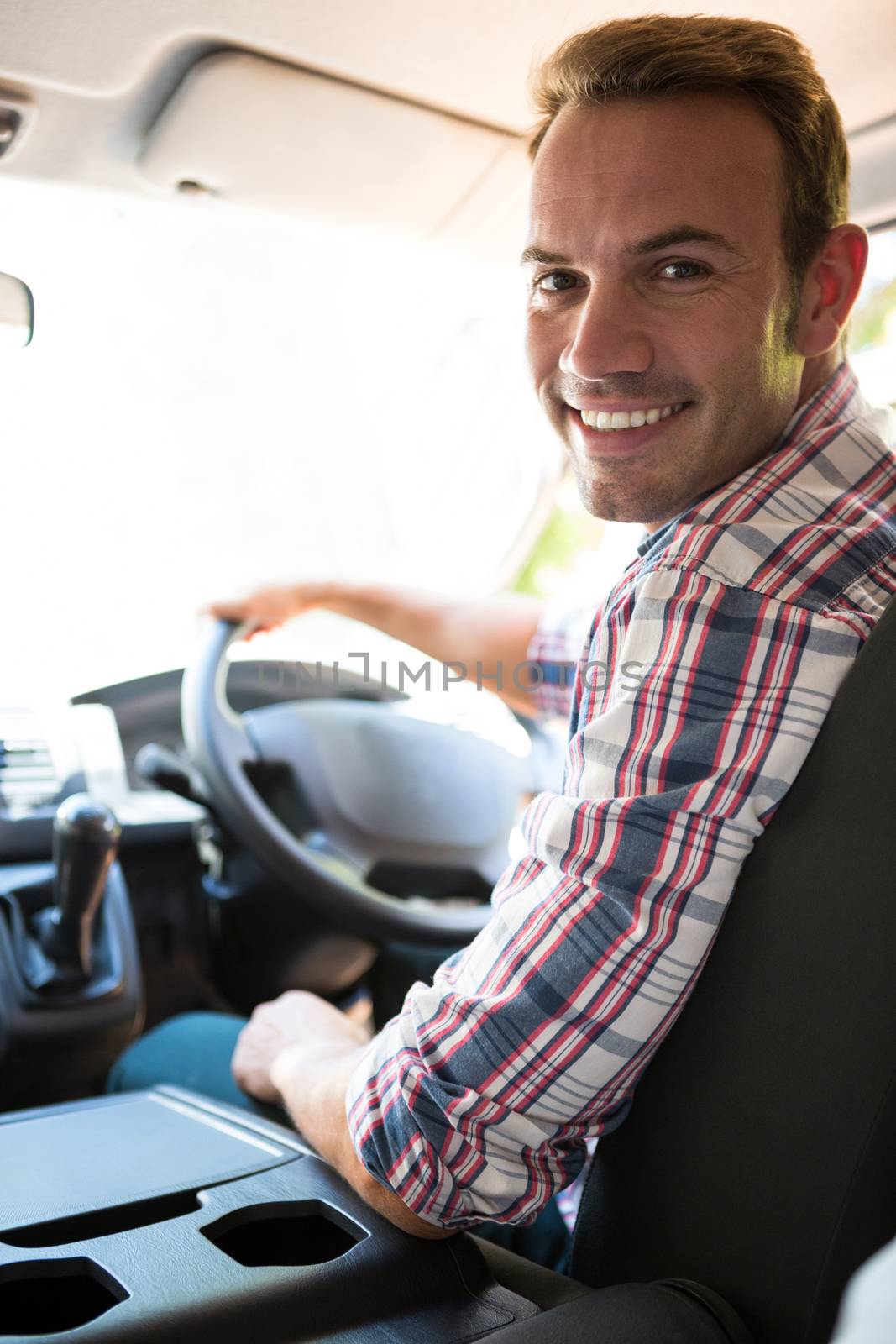 Portrait of young man looking at camera while sitting on cars front seat