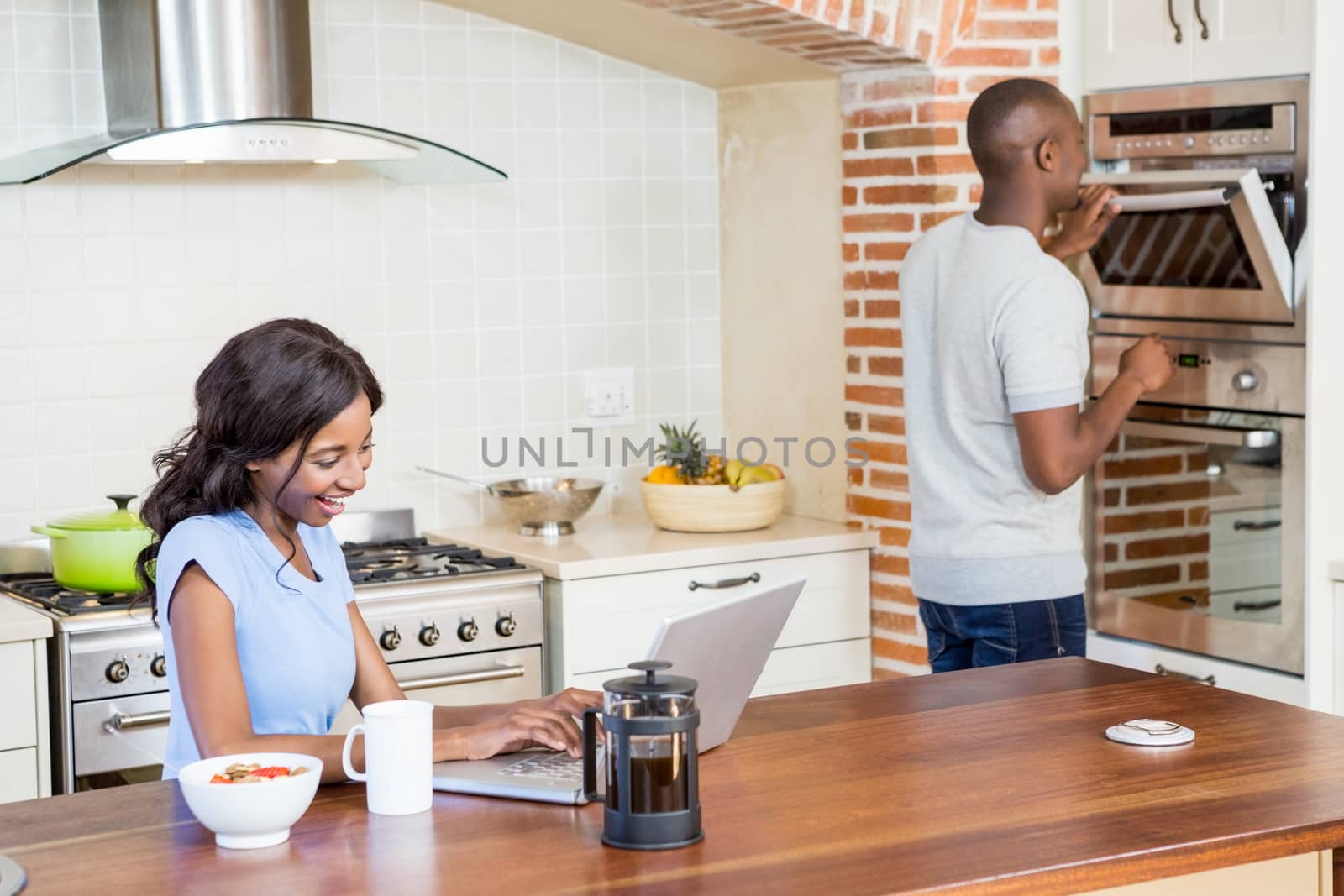 Young woman using laptop in the kitchen and man checking oven