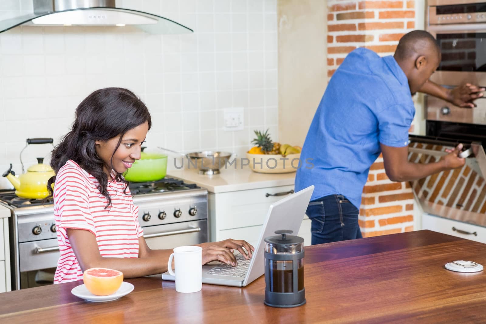 Young woman using laptop in the kitchen and man checking oven