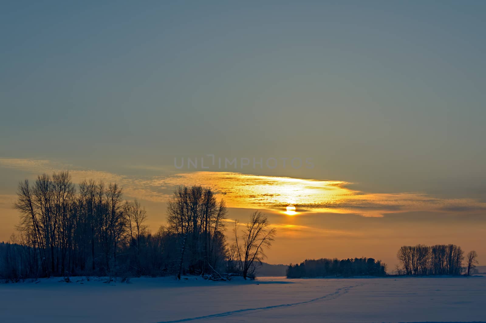 Orange low sun in a cloudy haze over the frozen river and islands.