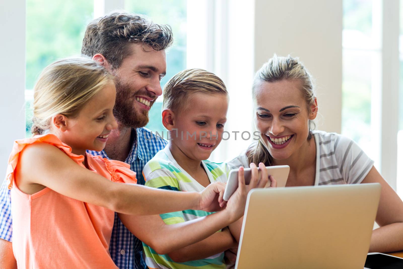 Children showing phone to parents sitting with laptop at table  by Wavebreakmedia
