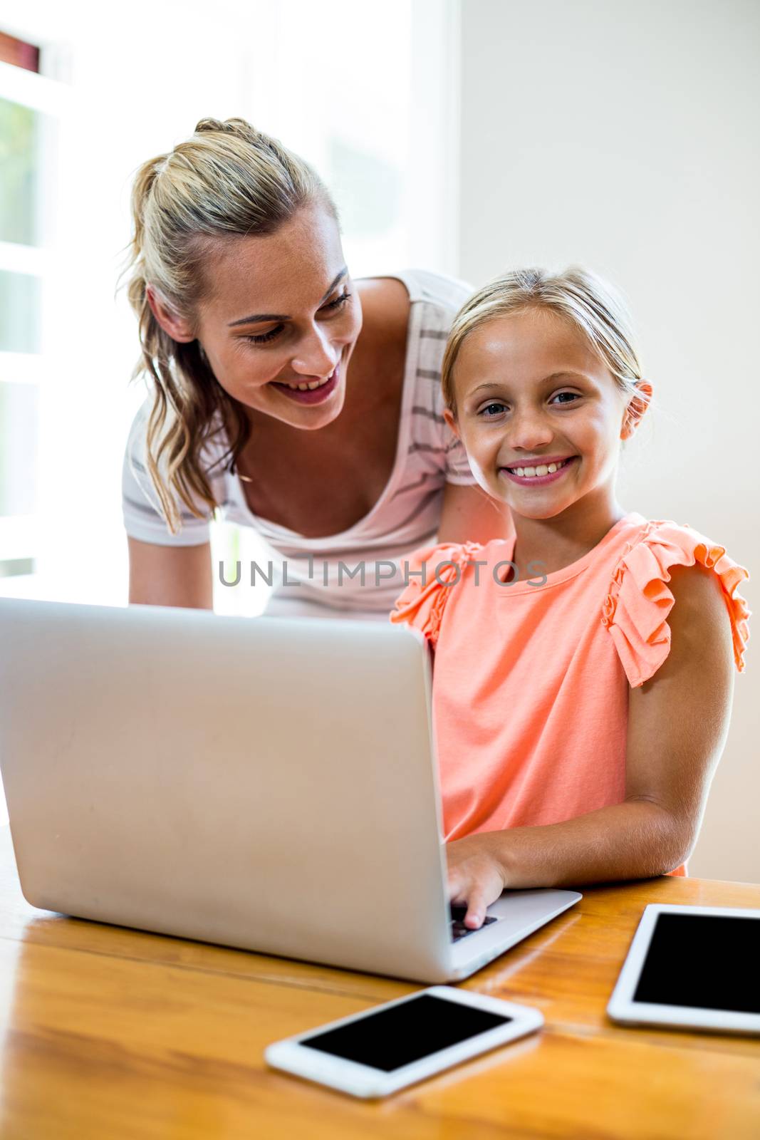 Mother teaching smiling daughter while using laptop at home 