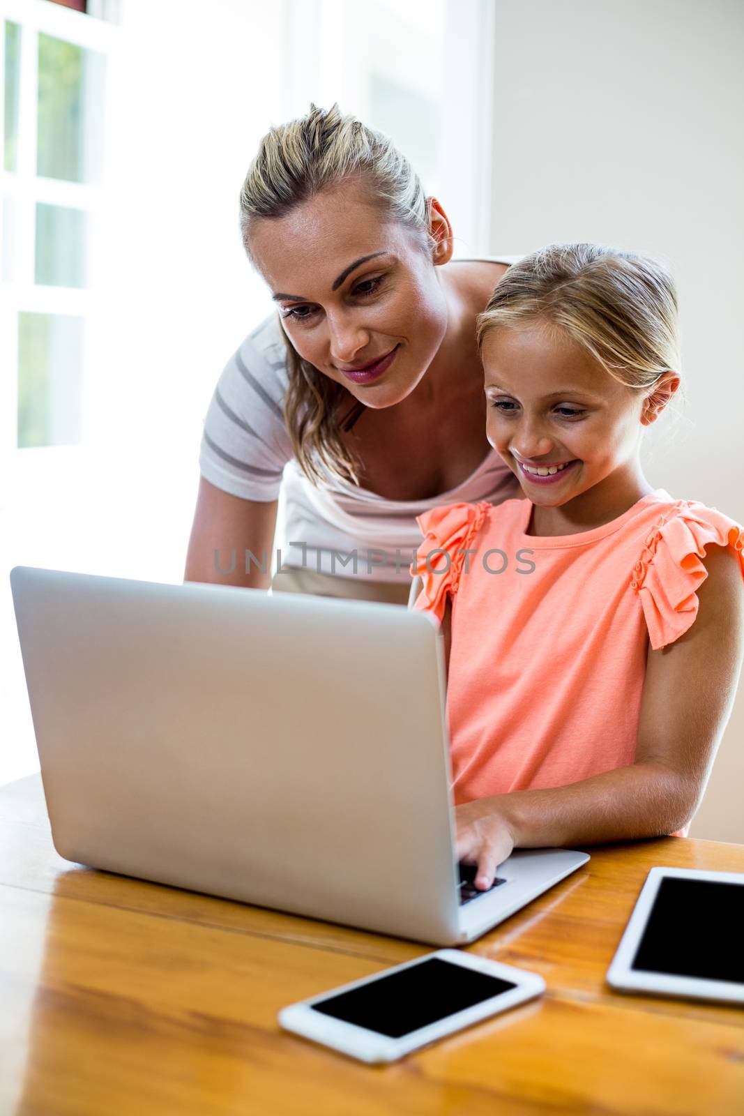 Mother assisting daughter in uising laptop at home  by Wavebreakmedia