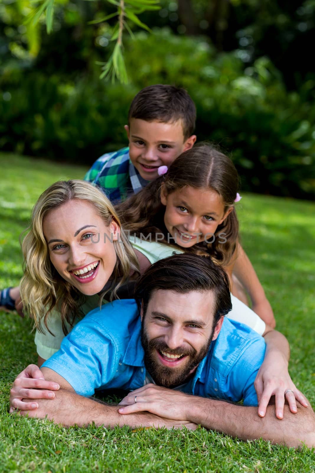 Portrait of smiling family lying on top of each other in yard 