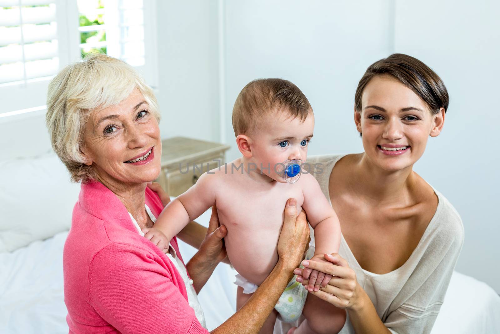 Happy grandmother and mother with baby boy on bed at home