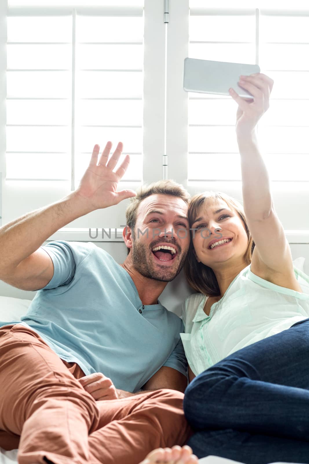 Cheerful couple taking selfie while relaxing on bed at home