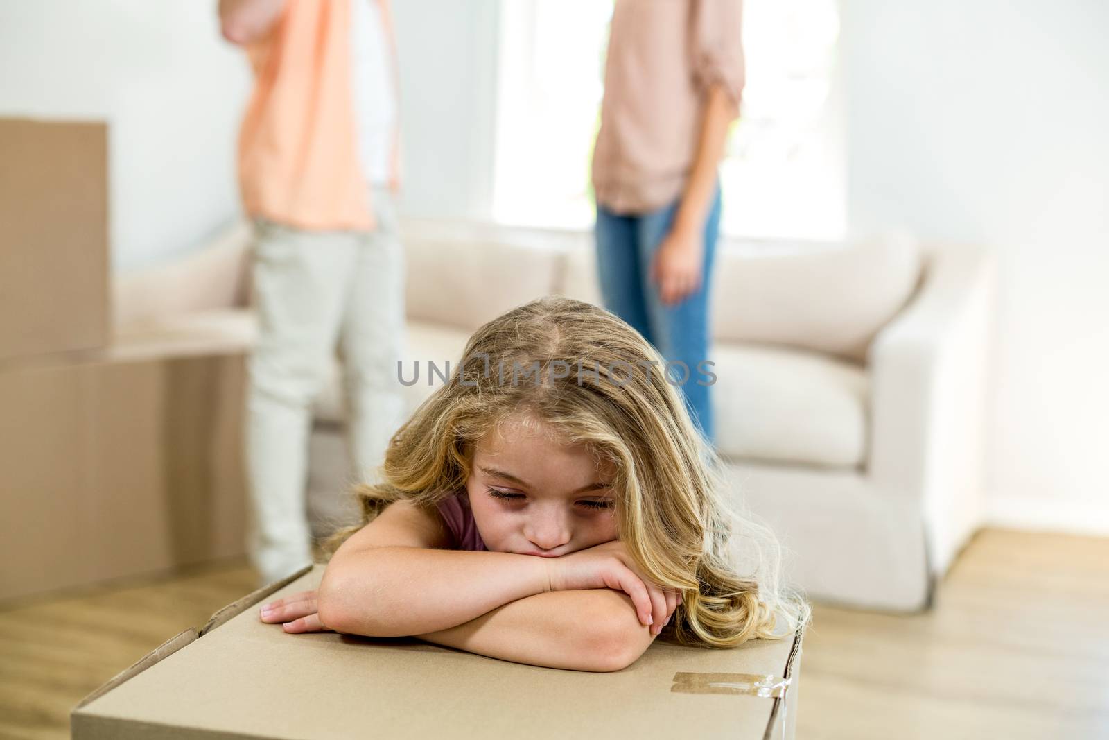 Close-up of upset girl leaning on box while parents standing in background