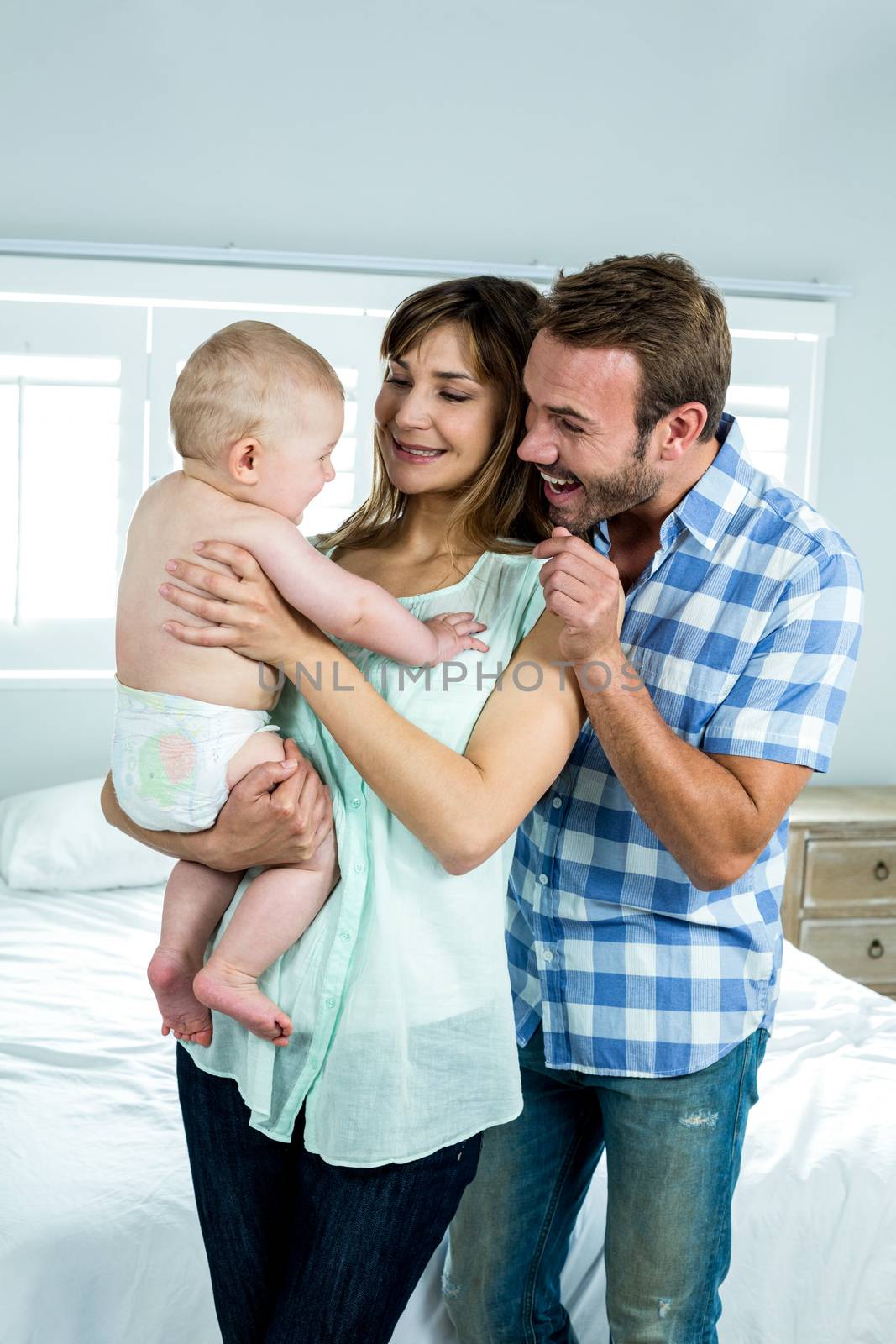 Cheerful parents with cute son by bed at home