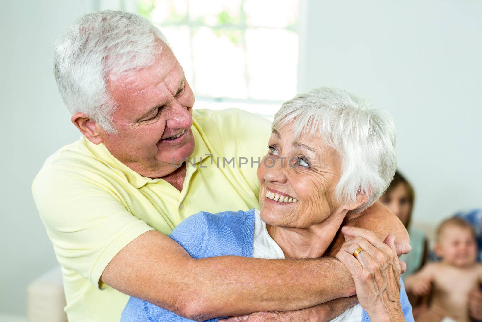 Close-up of happy couple embracing while family in background at home