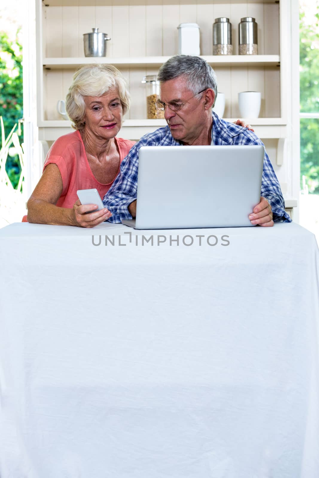 Senior couple using laptop and mobile phone in kitchen at home