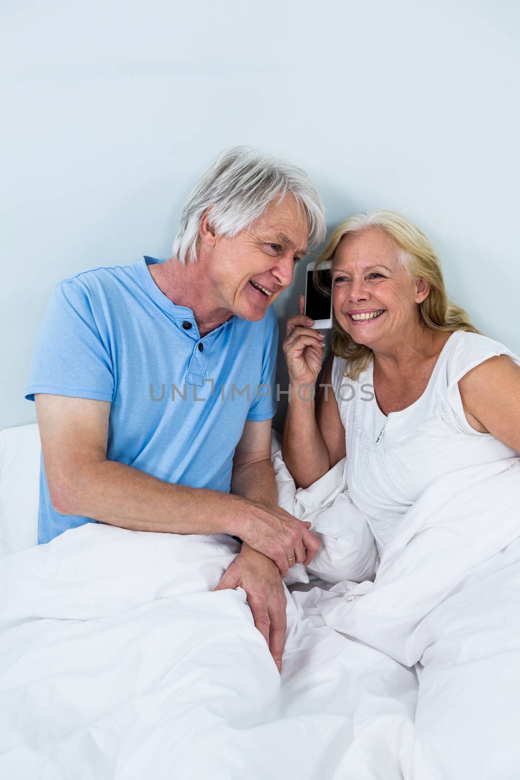Happy retired couple listening to music through smartphone while sitting on bed 