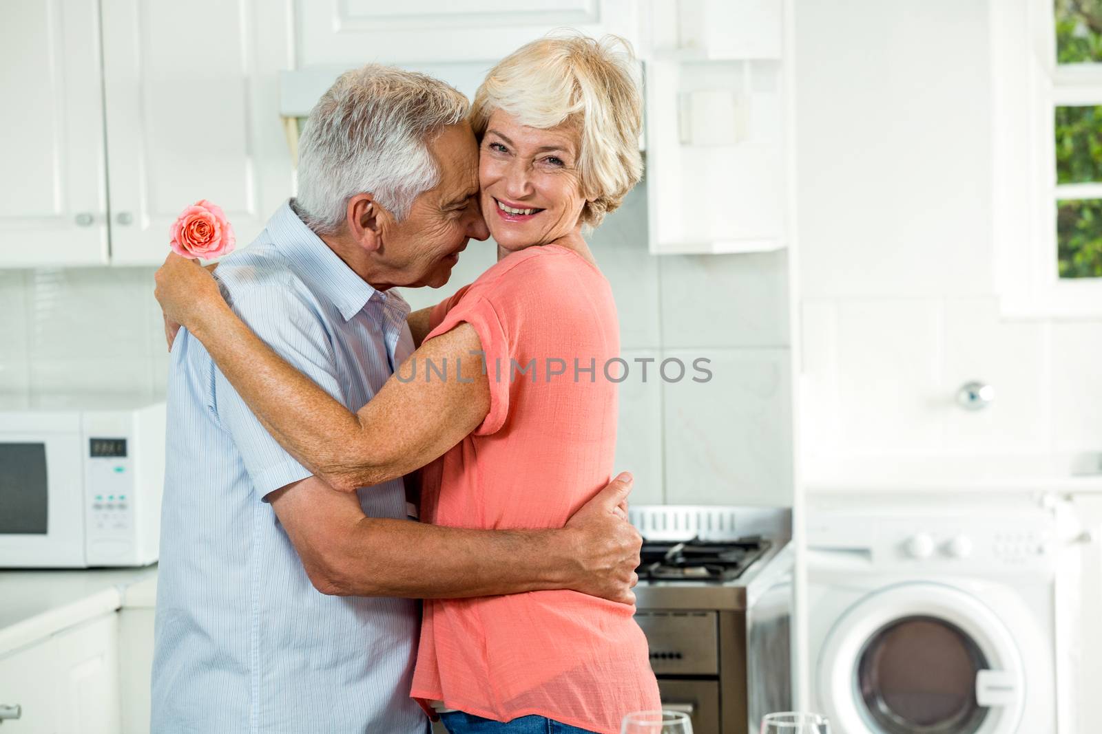 Romantic senior couple with rose while standing in kitchen