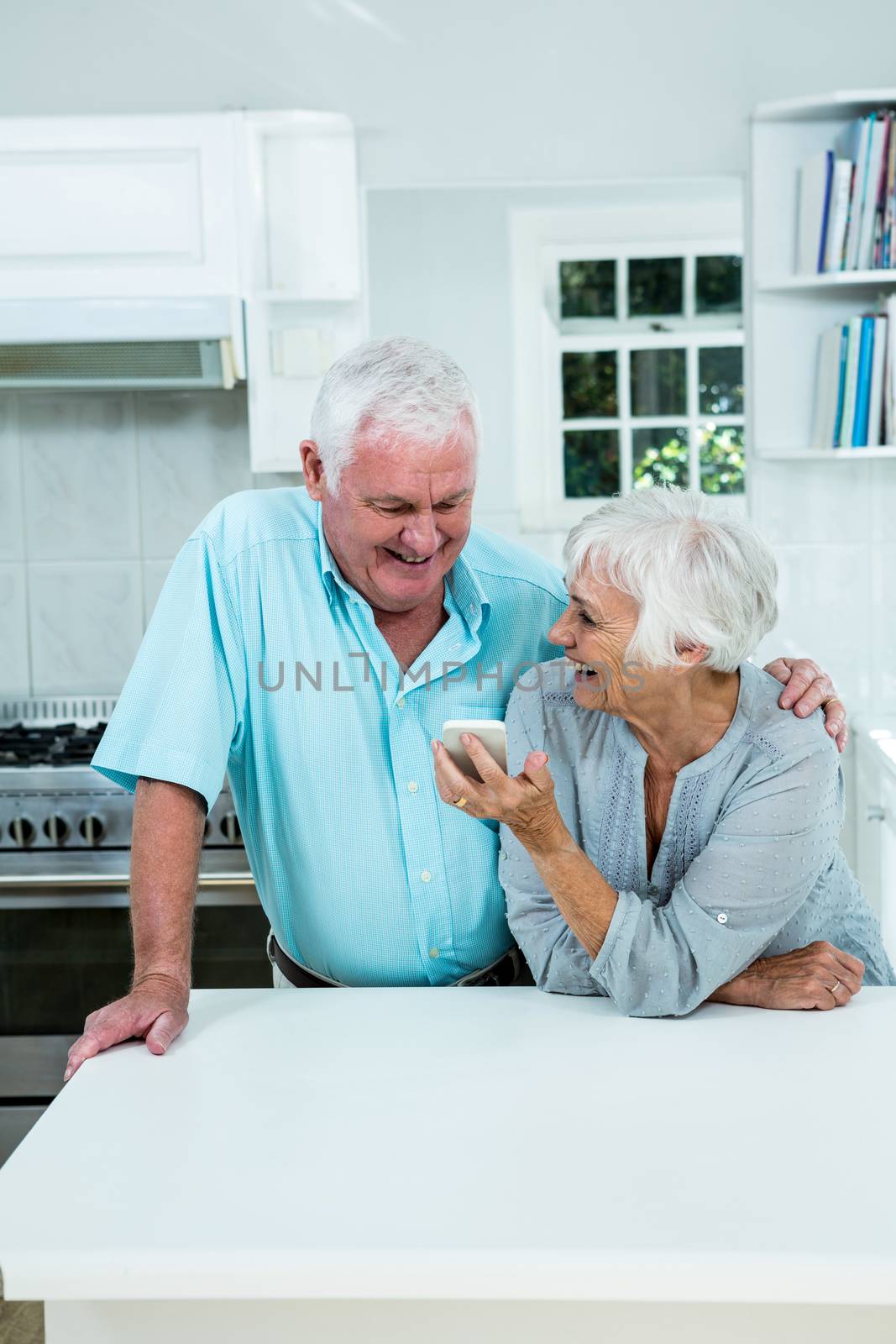 Smiling senior woman showing phone to man while standing in kitchen