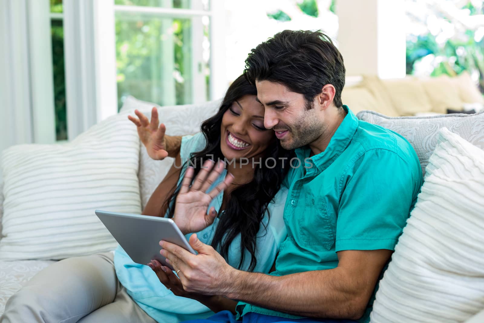 Couple waving hands while using digital tablet for video chat by Wavebreakmedia