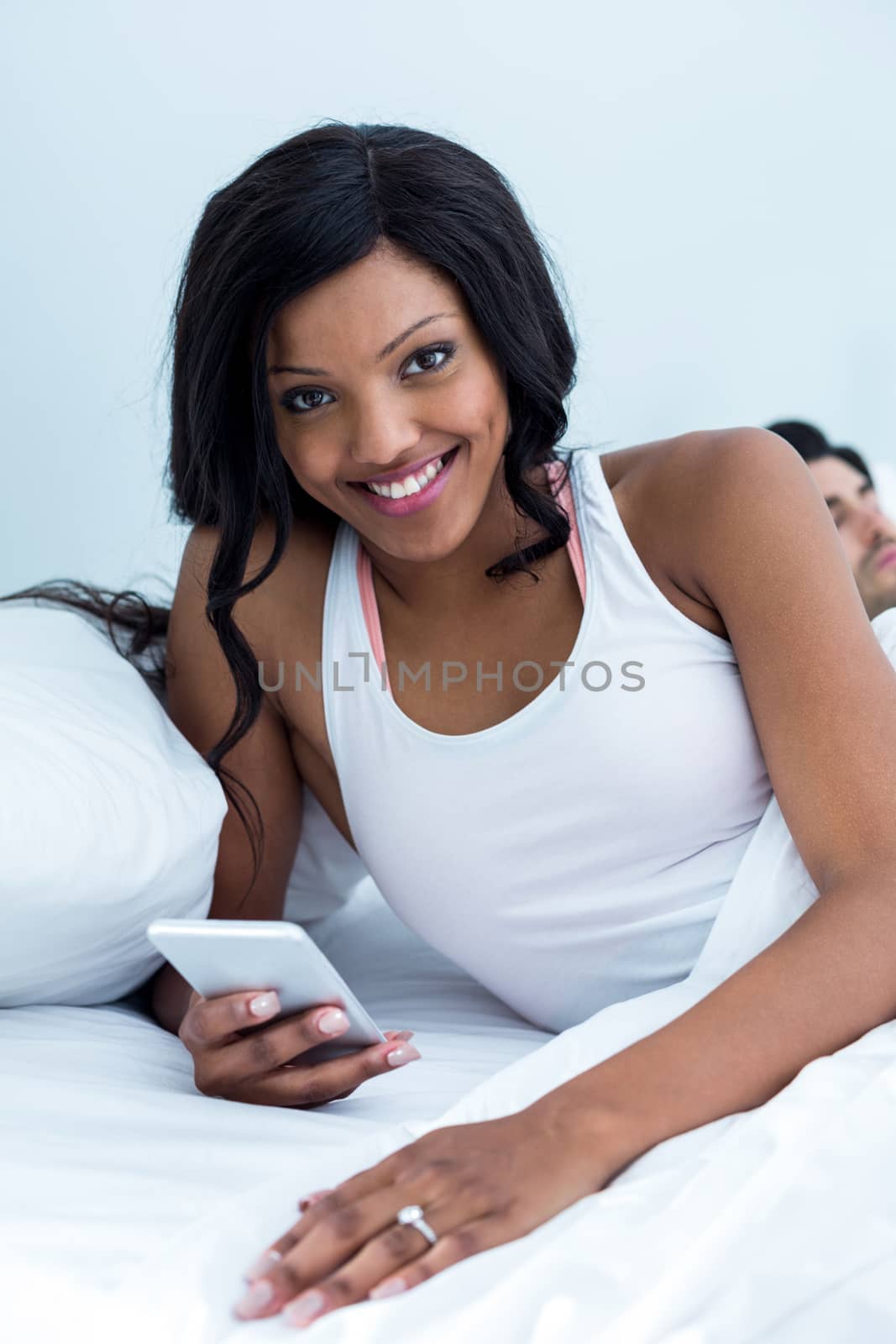 Woman using mobile phone while man sleeping on bed in bedroom