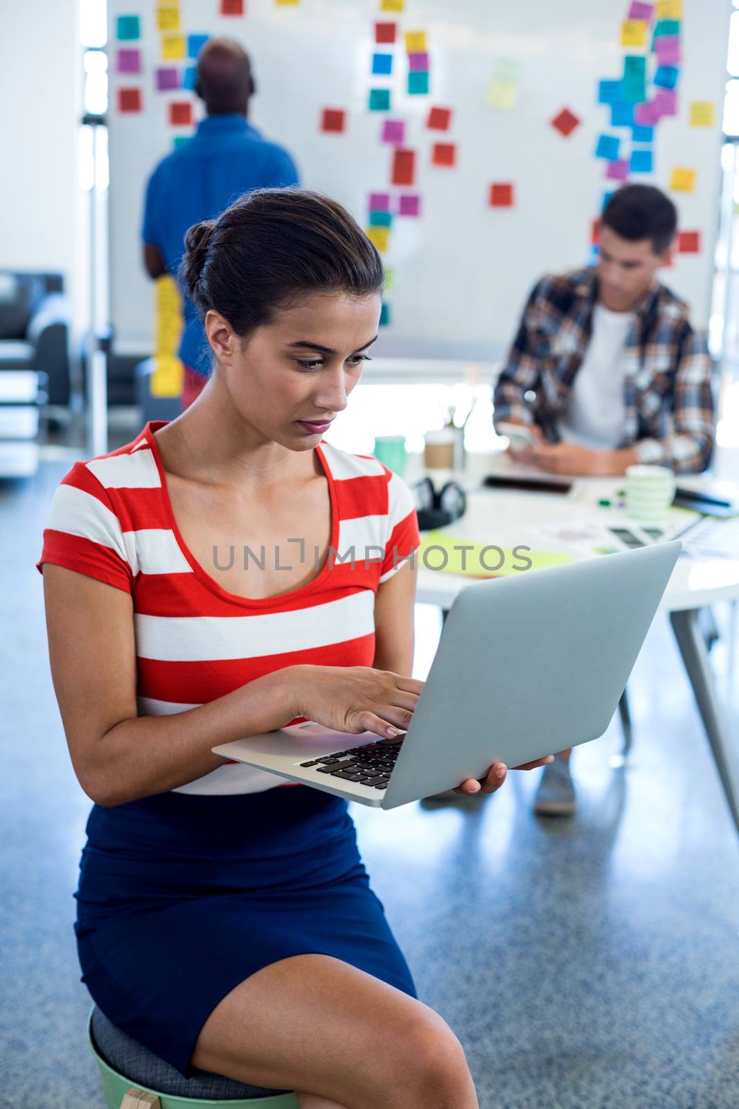 Young woman using laptop while colleagues working in the background