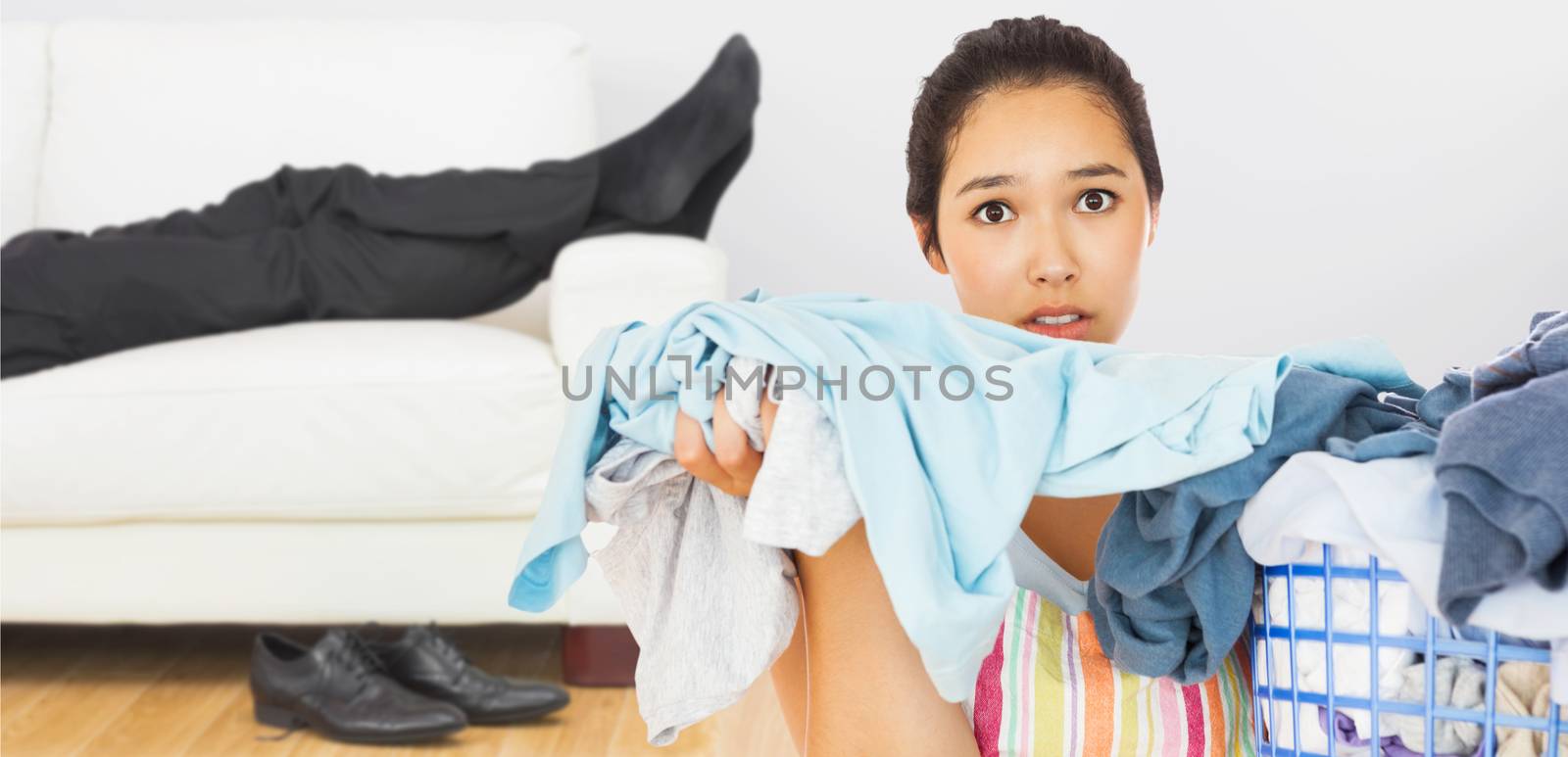 Frowning woman taking out dirty laundry  against low section of businessman resting on sofa in living room