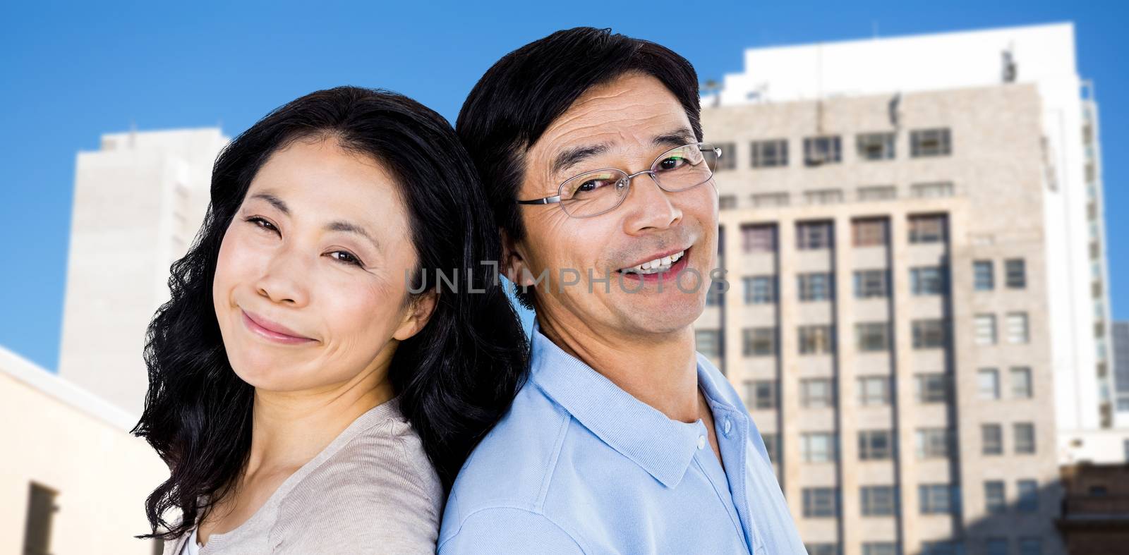Couple with their backs to each other against low angle view of city buildings