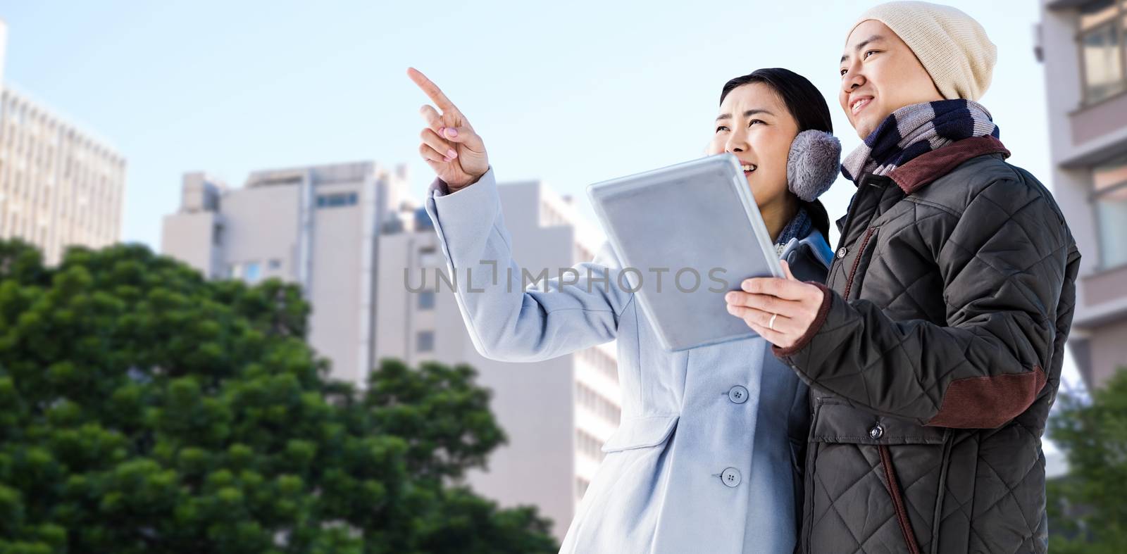 Couple looking away while holding digital tablet against low angle view of city buildings
