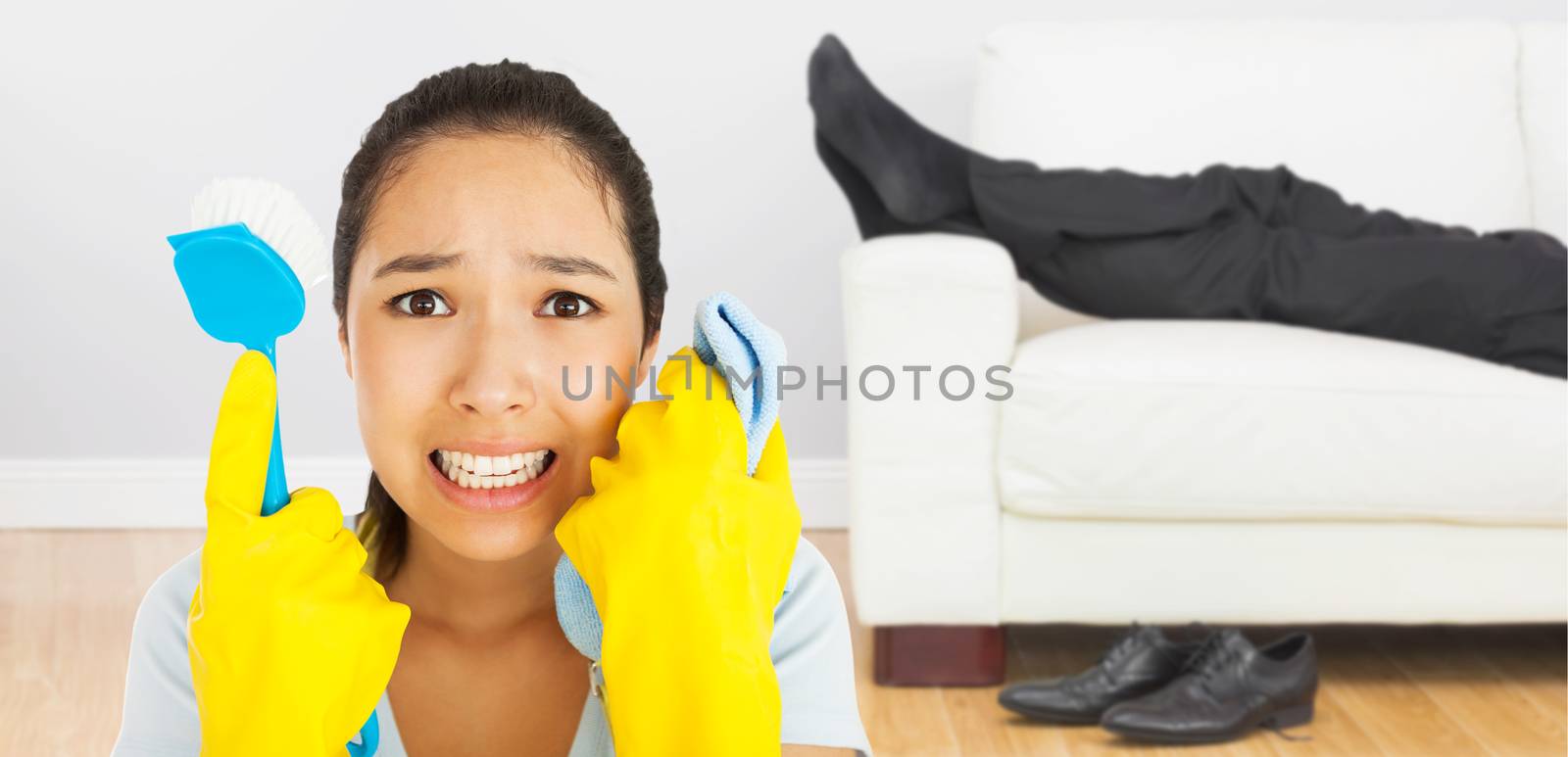 Distressed woman holding cloth and scrubbing brush against low section of businessman resting on sofa in living room