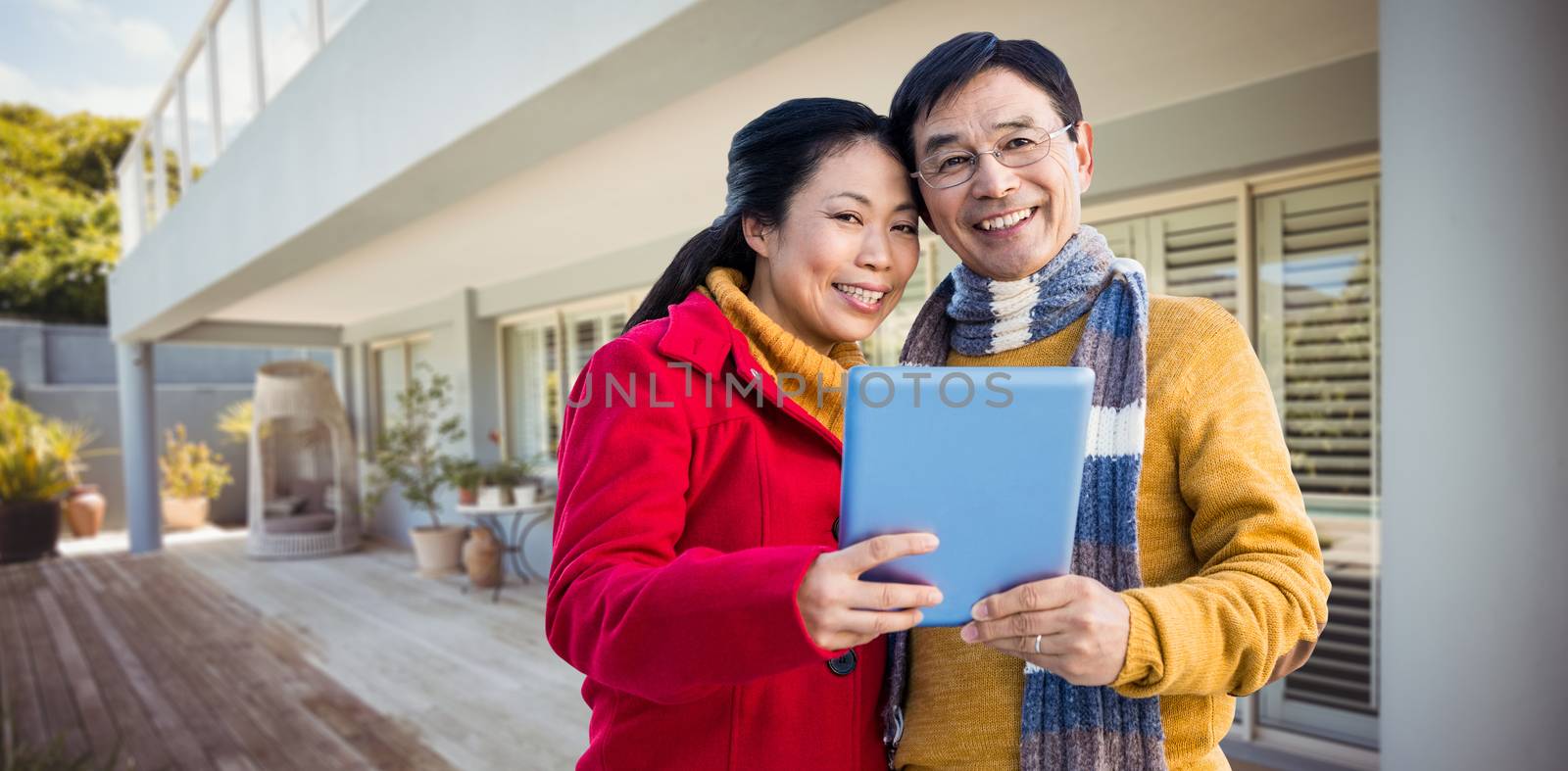 Asian couple on balcony using tablet against stylish outdoor patio area