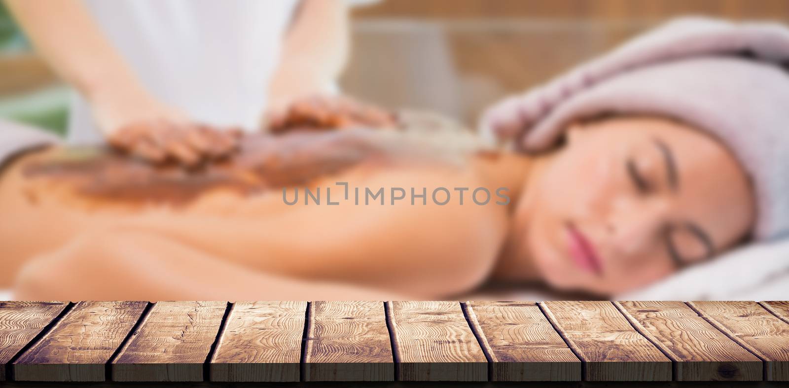 Attractive woman receiving chocolate back mask at spa center against wooden desk