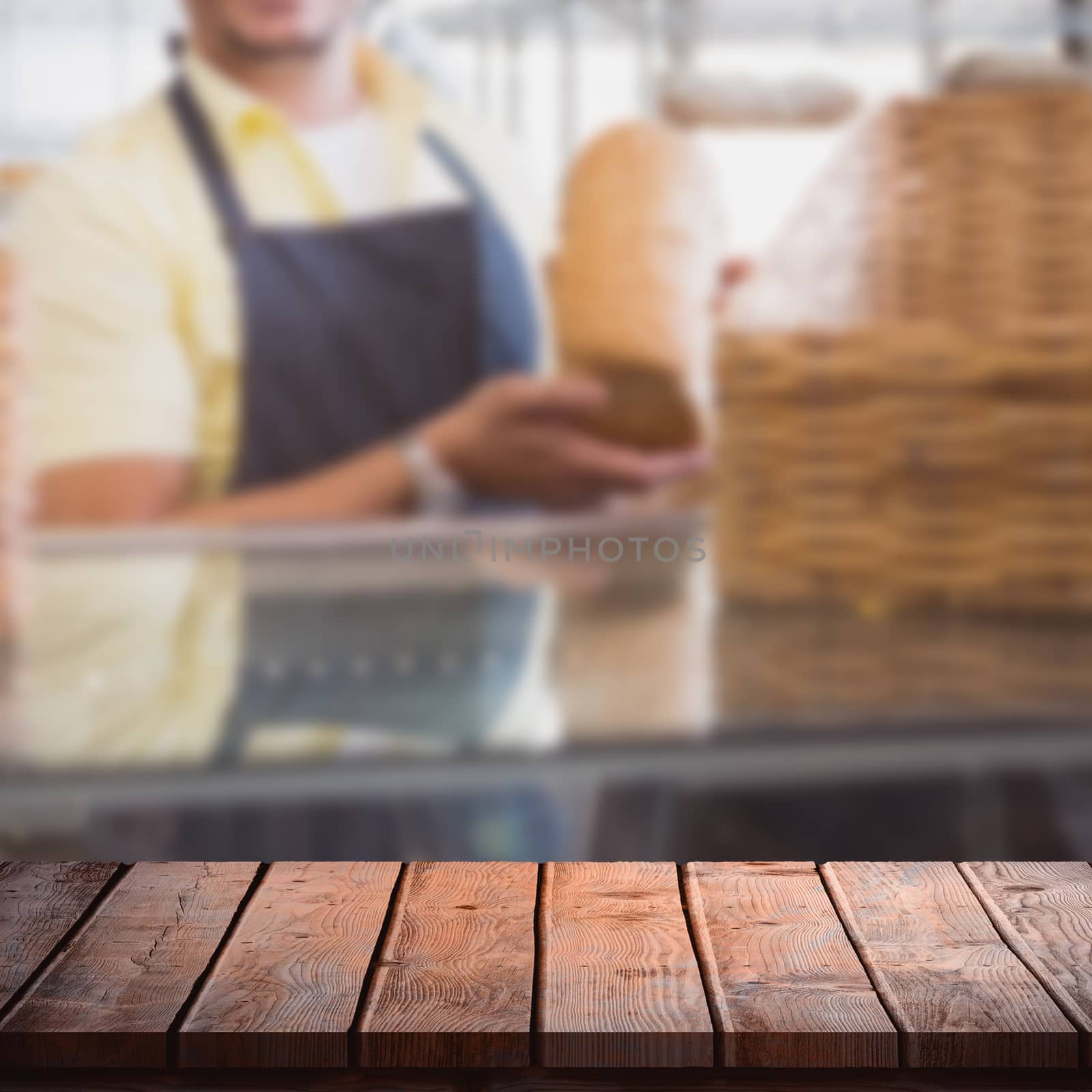 Wooden table against smiling worker showing a loaf 