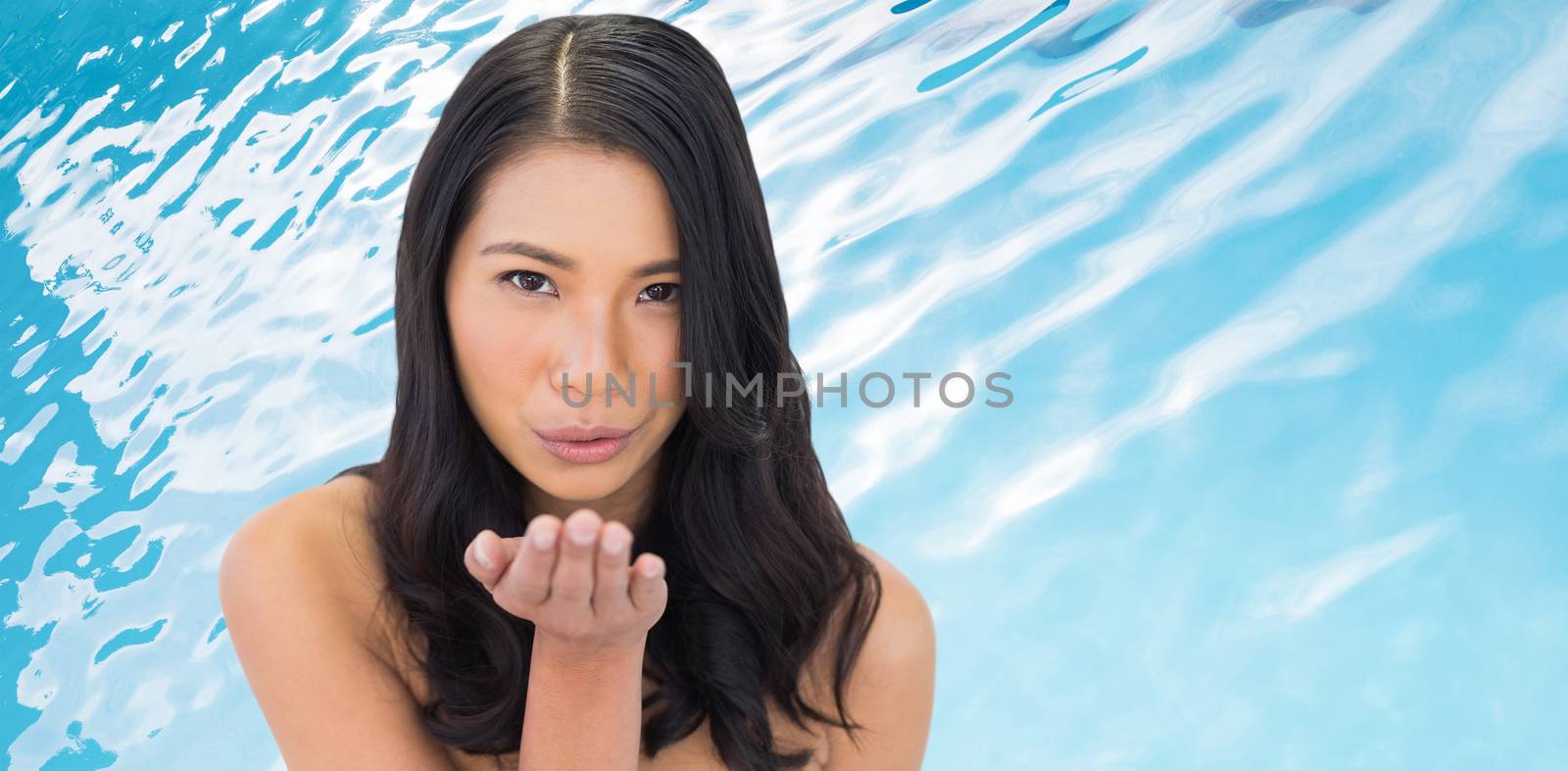Nude sensual dark haired model sending a kiss to camera against ripples on blue swimming pool