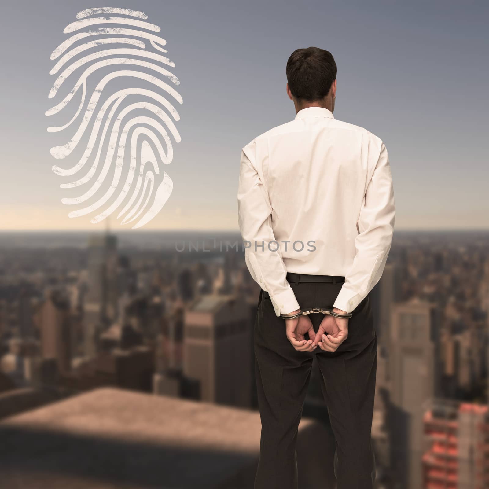 Rear view of young businessman wearing handcuffs against city skyline