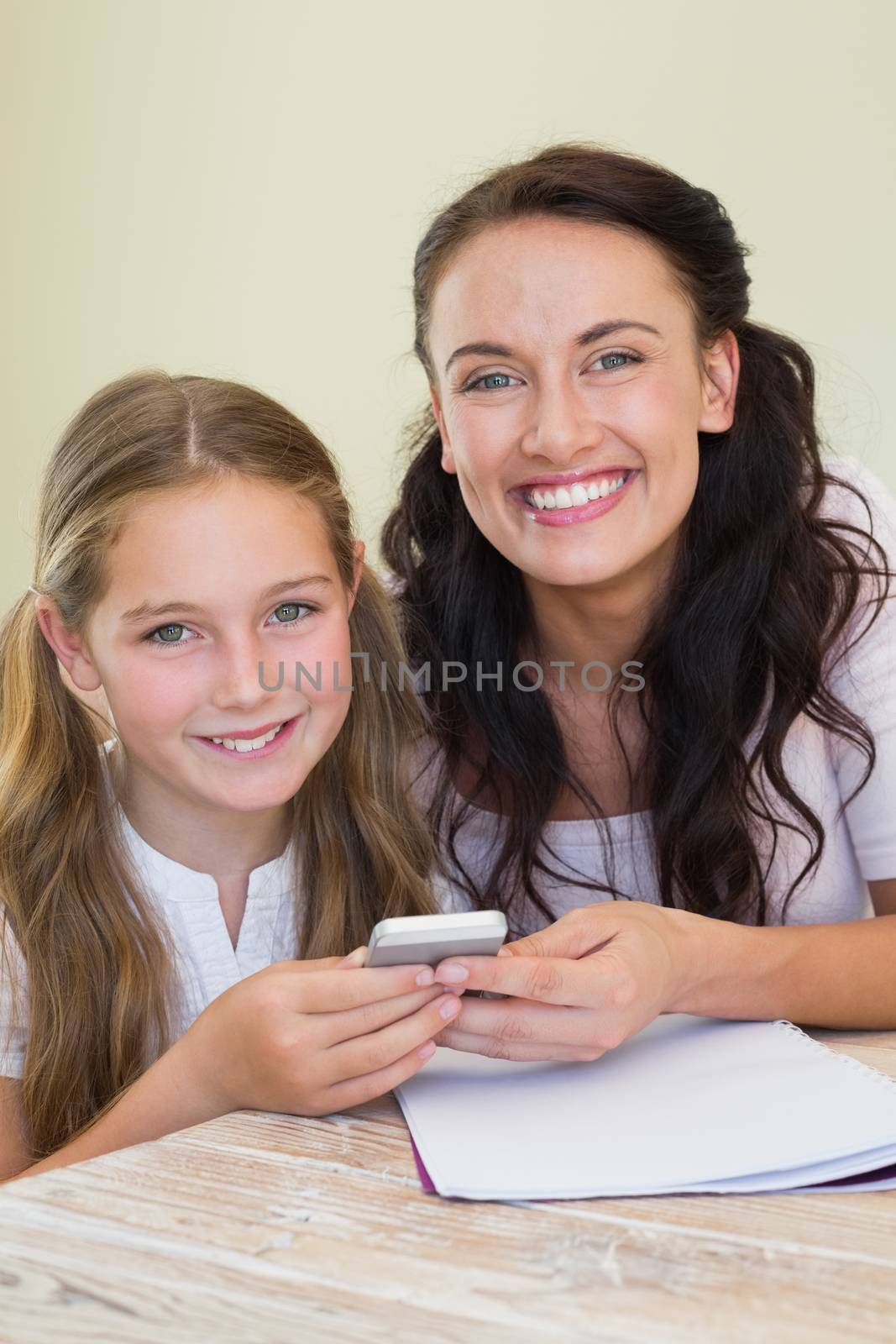 Portrait of happy mother and holding mobile phone at table in house