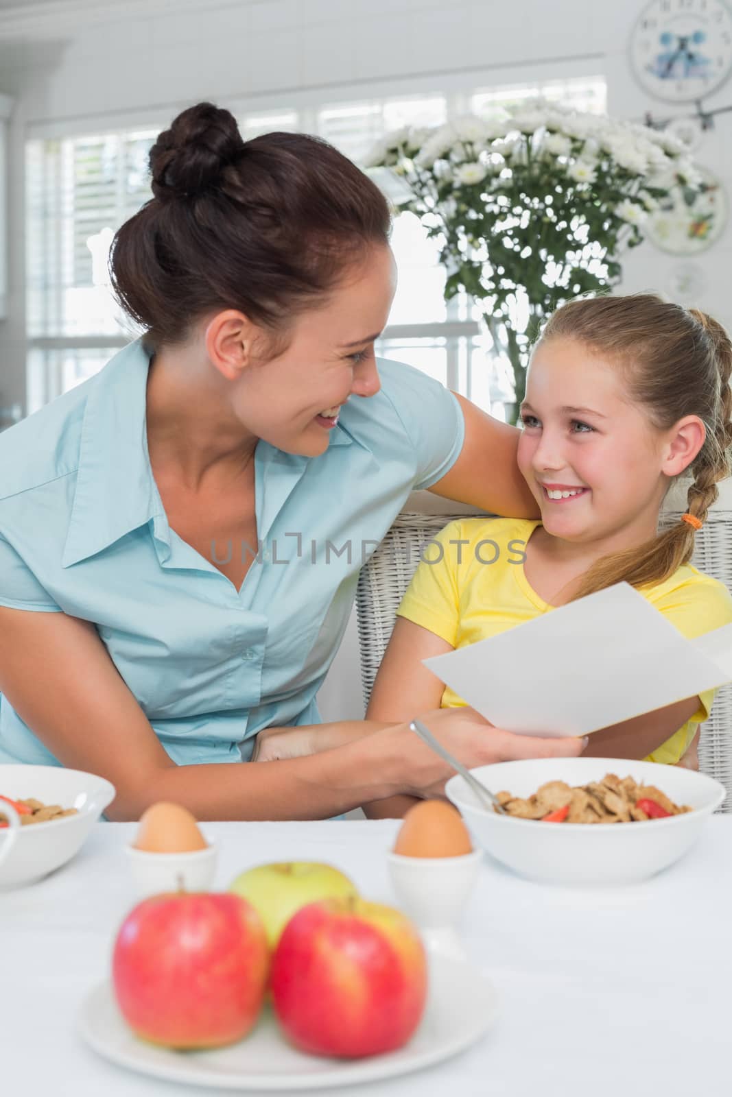 Mother and daughter with greeting card at breakfast table by Wavebreakmedia