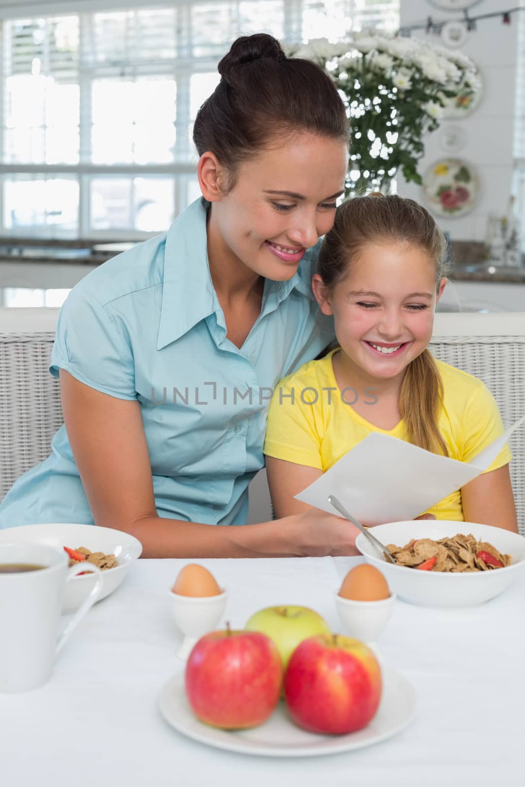 Happy mother and daughter reading greeting card at breakfast table