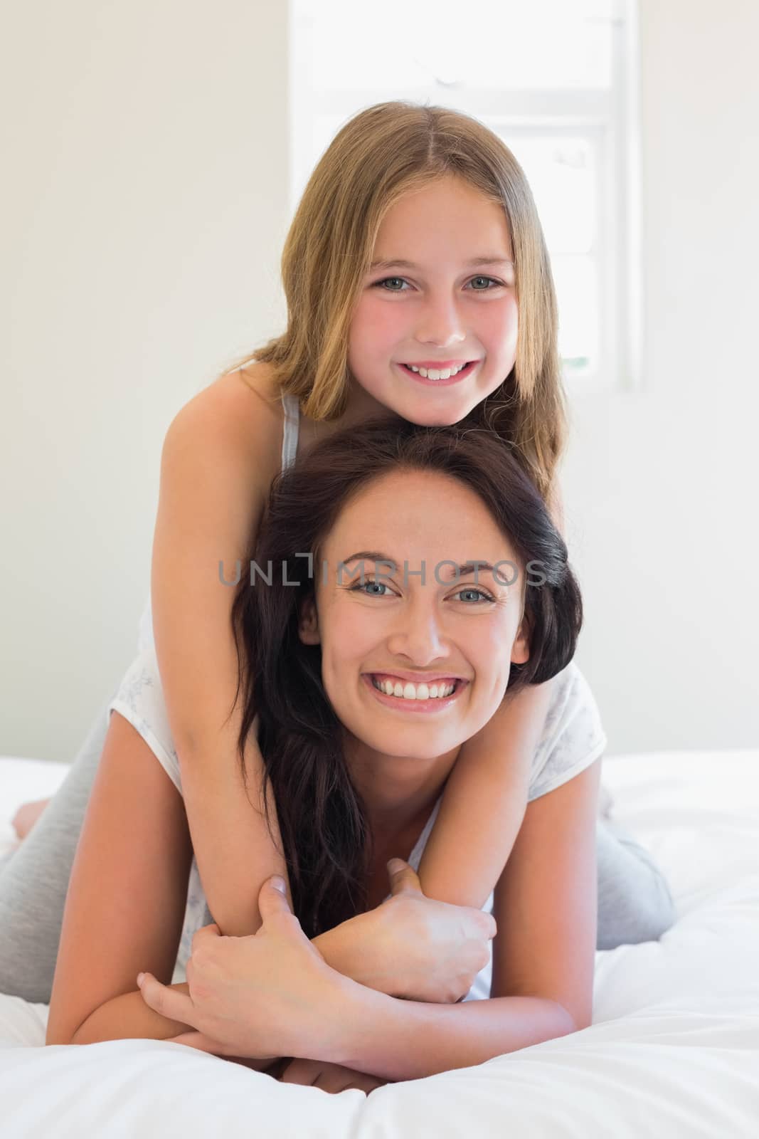 Portrait of happy girl sitting on mother in bedroom