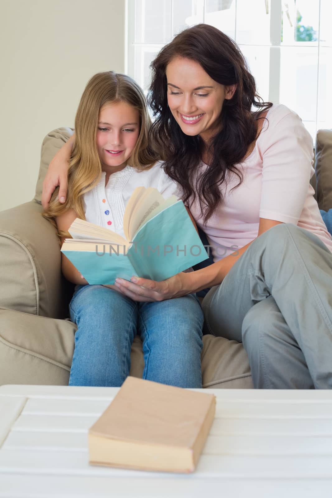 Girl and mother reading novel together on sofa at home