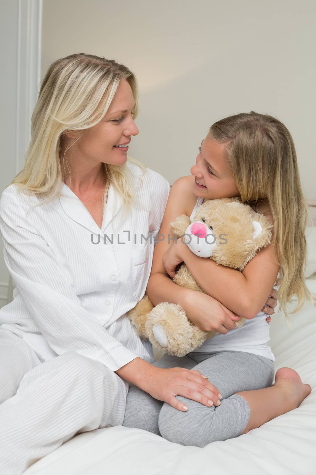 Girl embracing teddy bear while looking at mother in bed by Wavebreakmedia