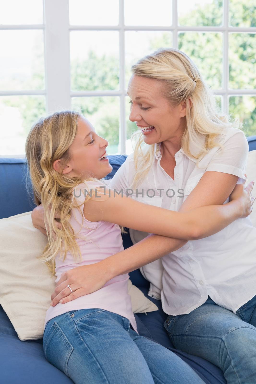 Excited mother embracing daughter while sitting on sofa in living room