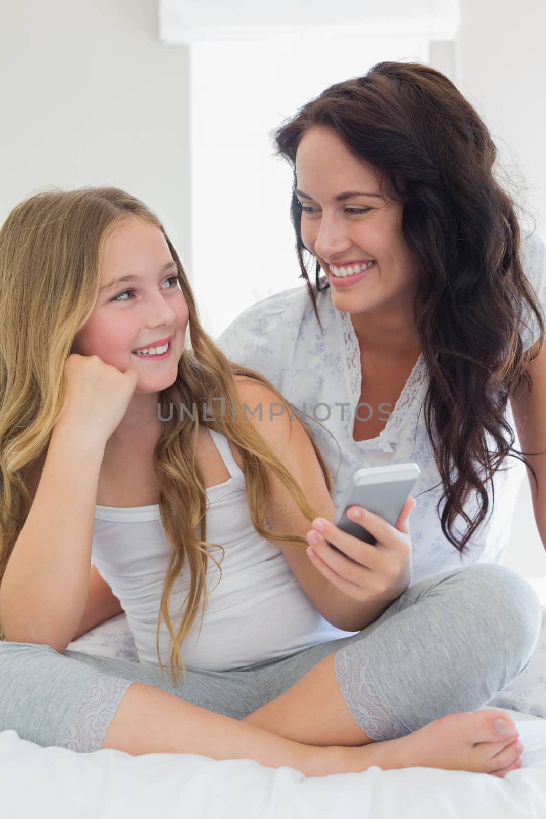 Happy mother and daughter with mobile phone looking at each other in bed