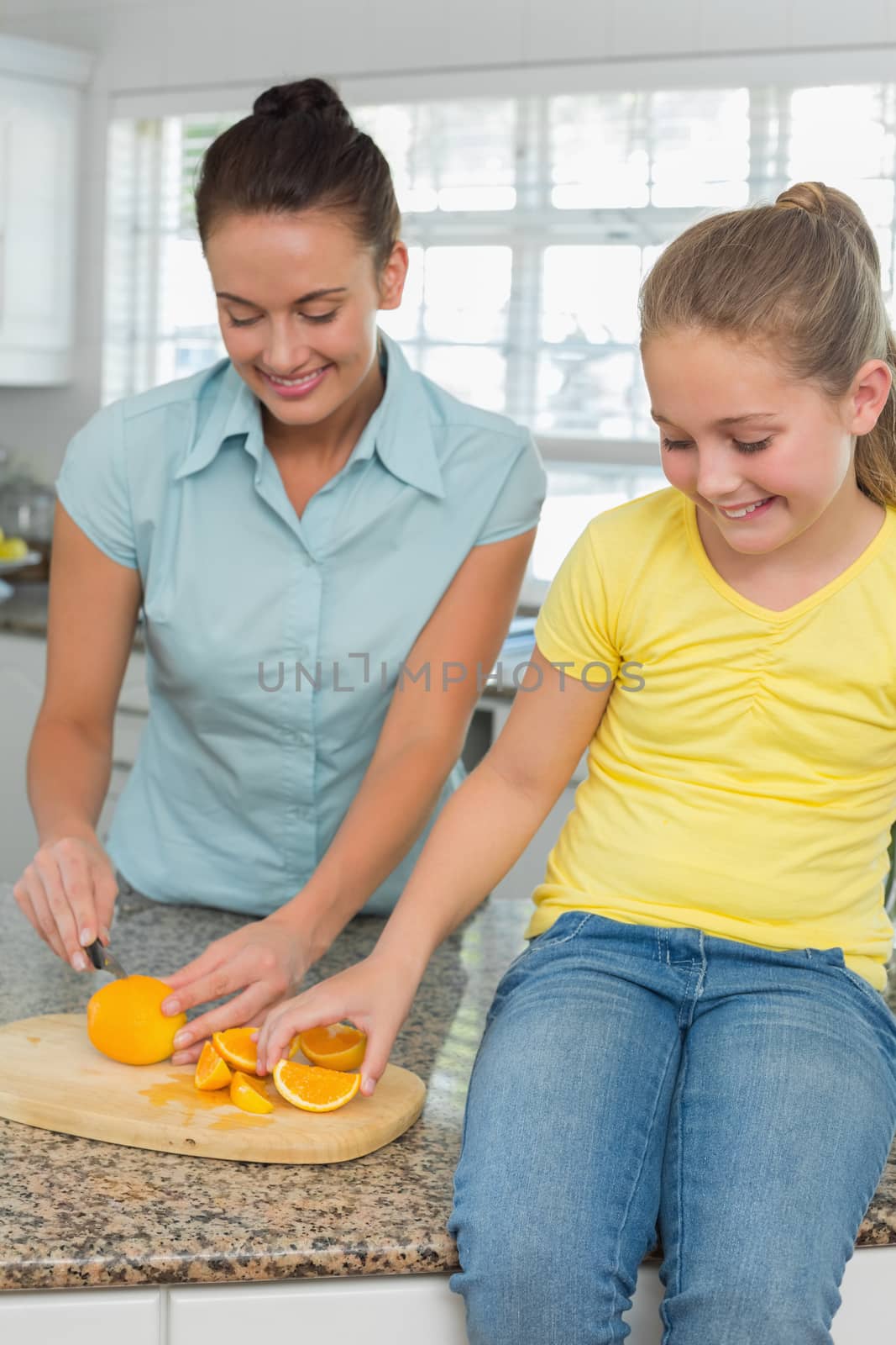Woman slicing oranges for daughter in kitchen by Wavebreakmedia