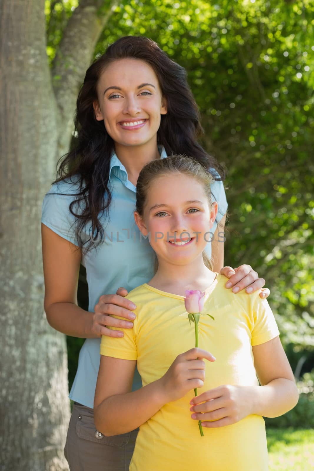 Portrait of cute girl holding rose while standing with mother in park
