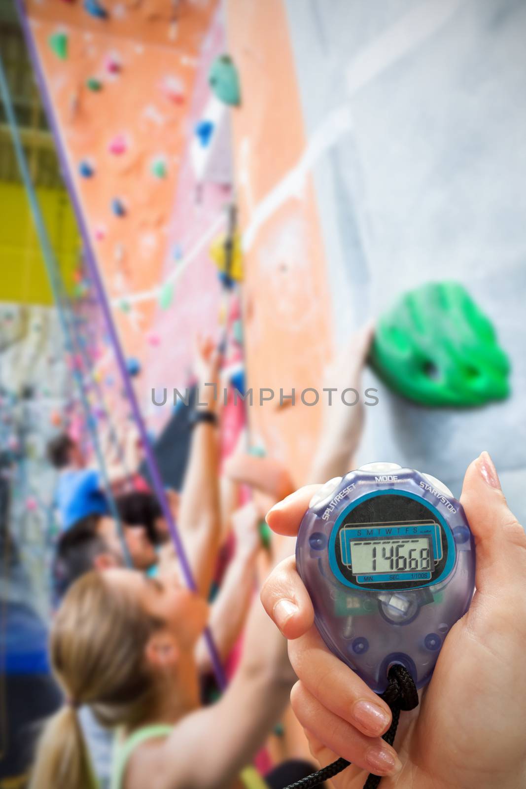 Close up of a hand holding a timer on a white background against fit people rock climbing indoors