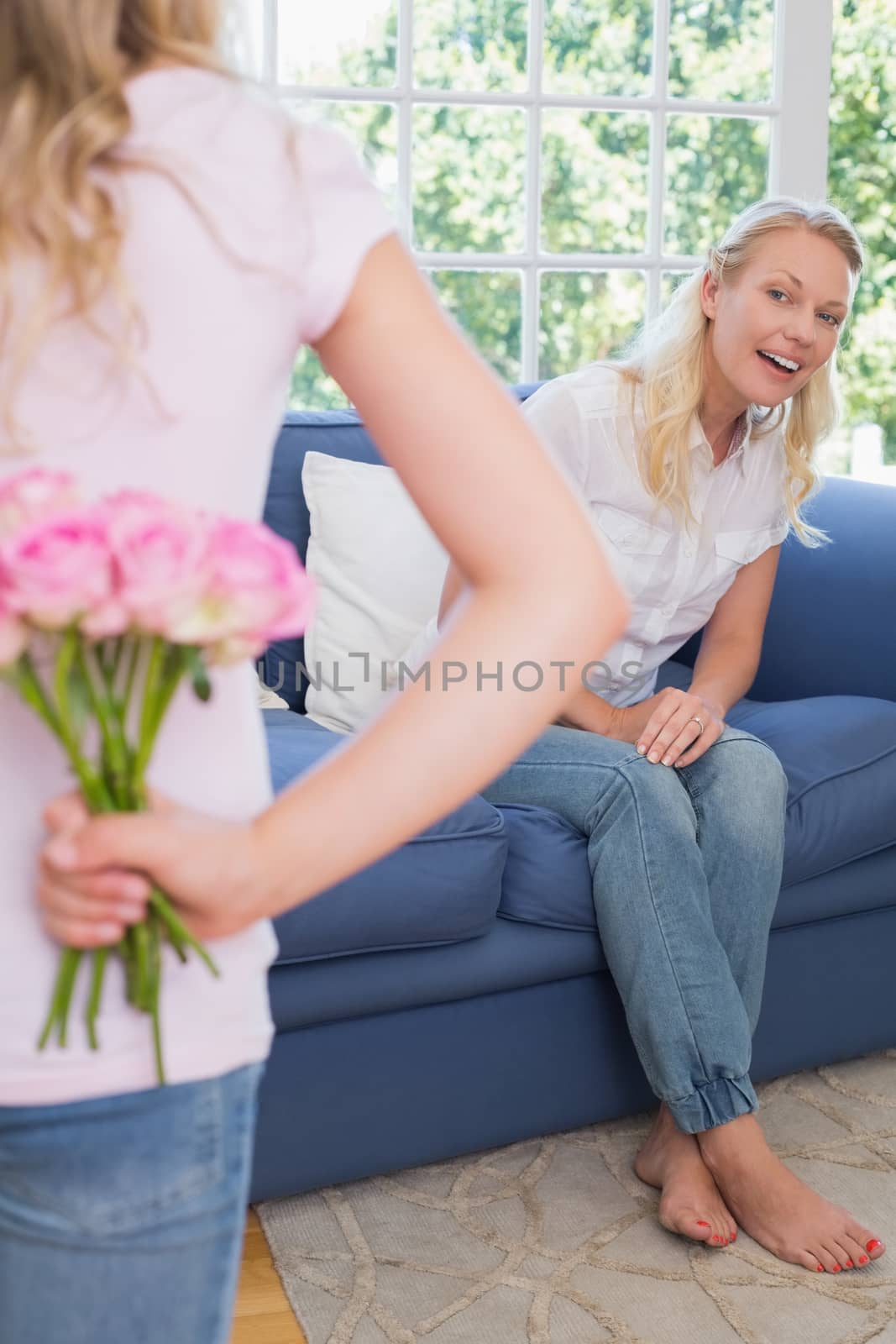 Happy mother looking at girl hiding flowers behind back at home